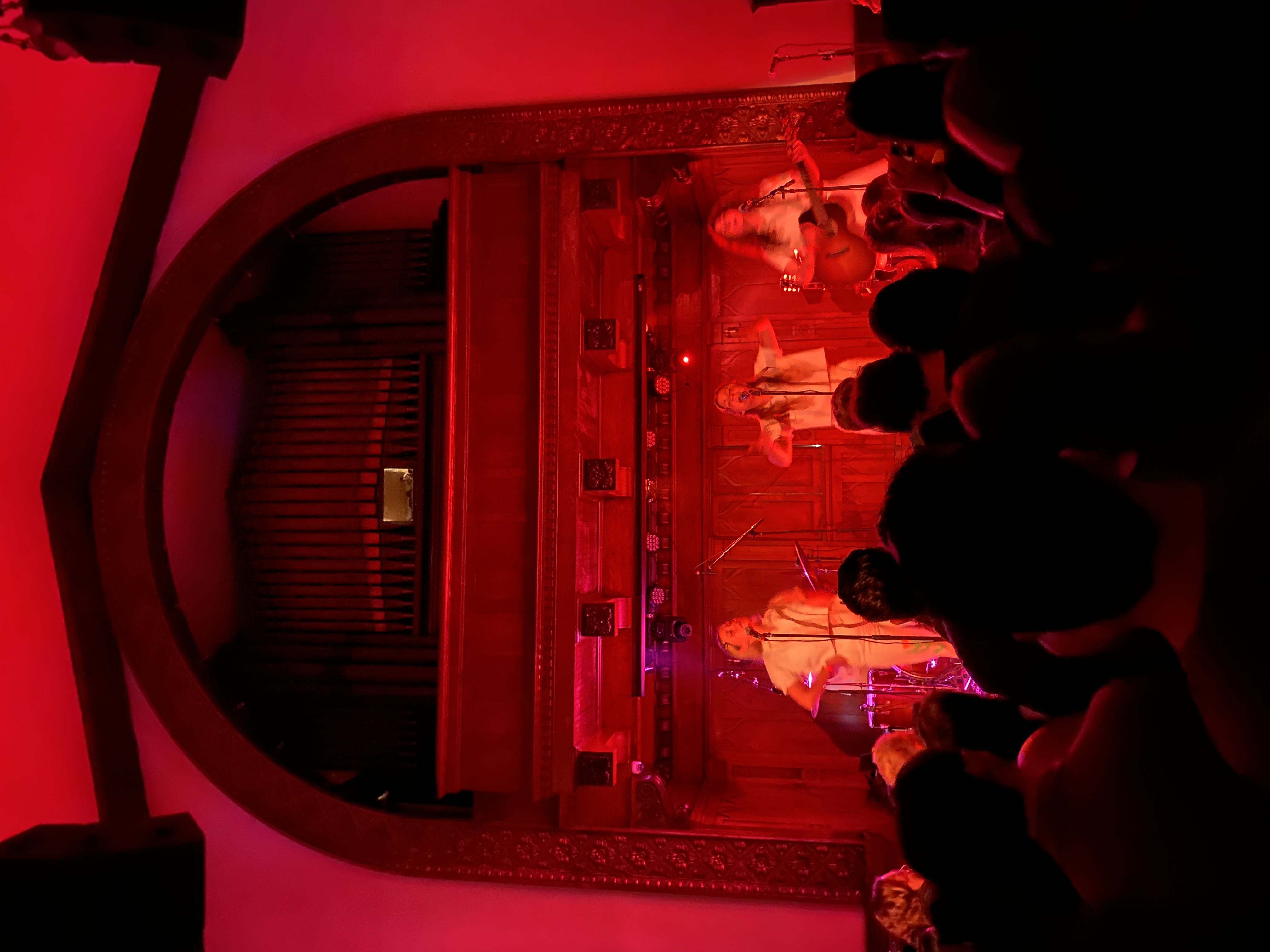 Band performing in church venue with dramatic red lighting and organ pipes