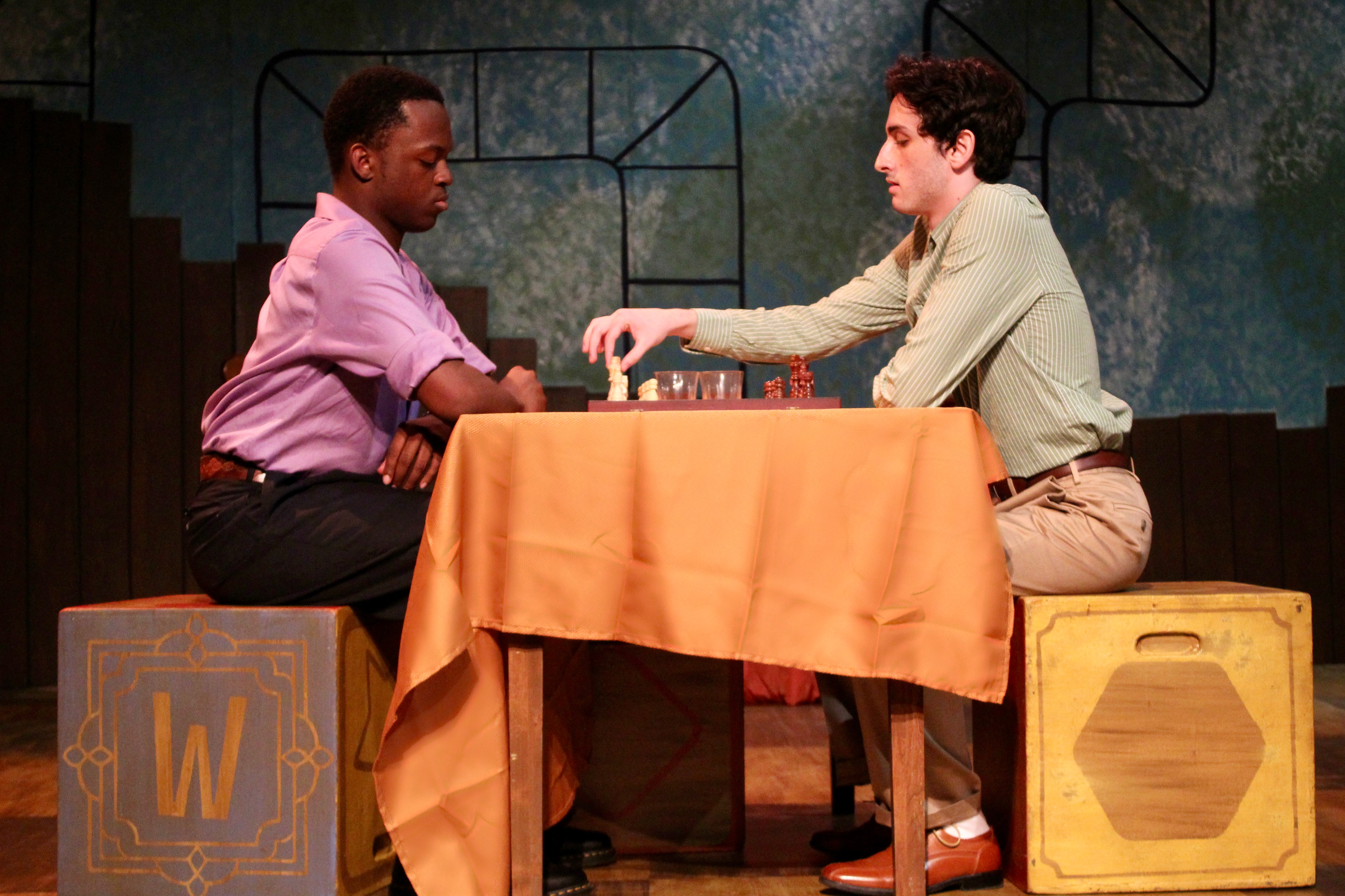 Falsettos - Two men playing chess on alphabet block seats