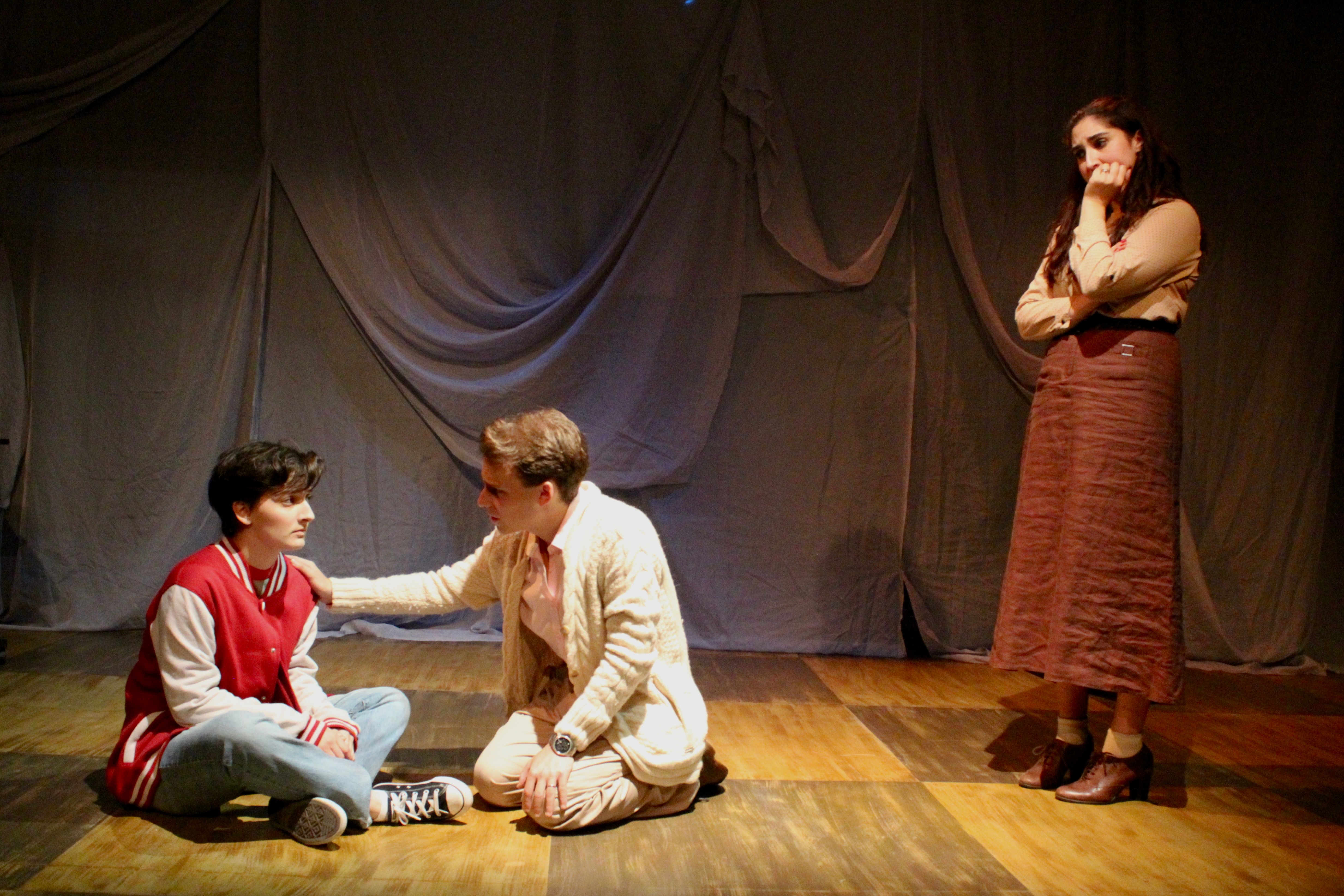 Falsettos - Three actors on floor with draped backdrop, varsity jacket scene