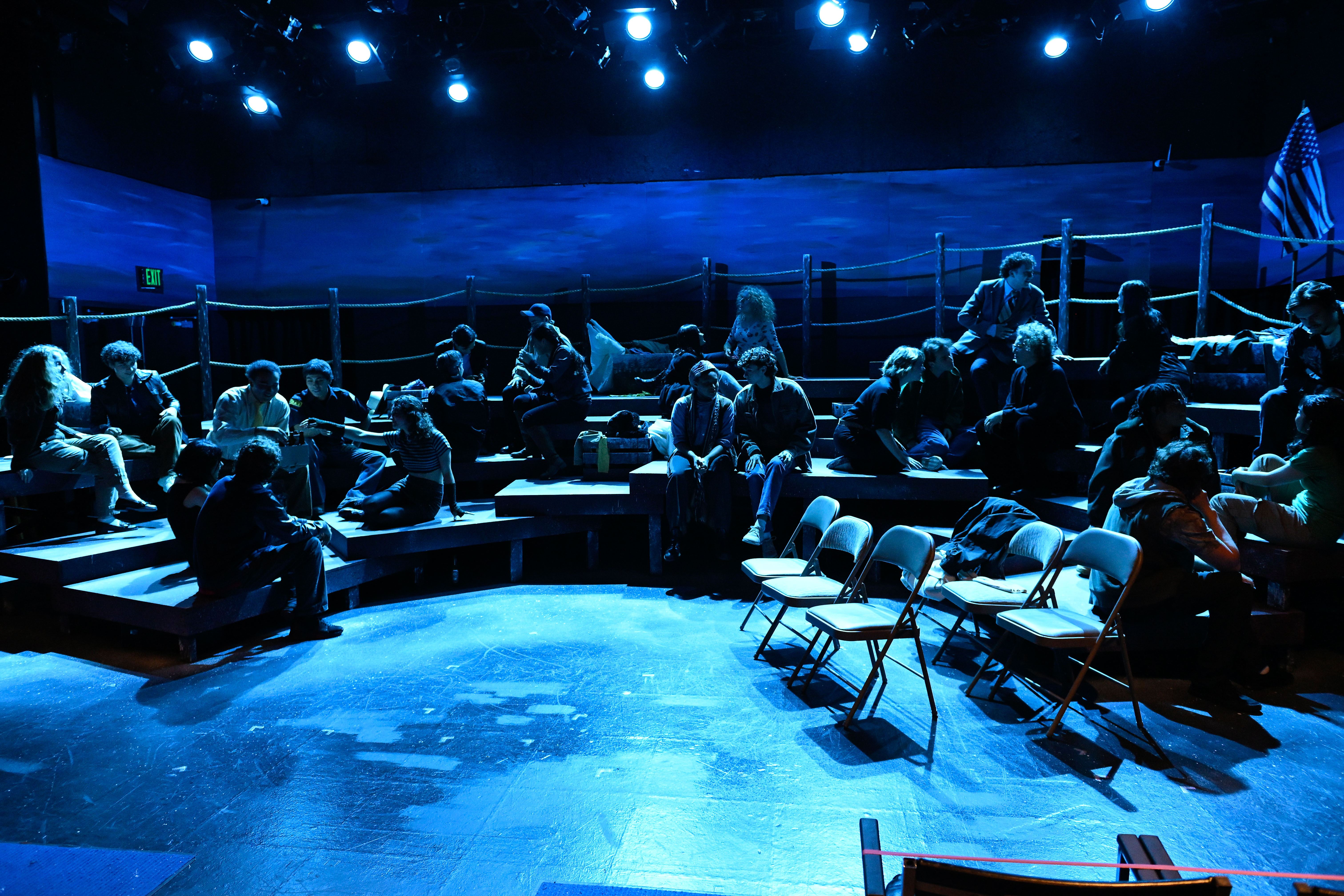 The Laramie Project - Full cast on tiered platforms with dramatic blue lighting