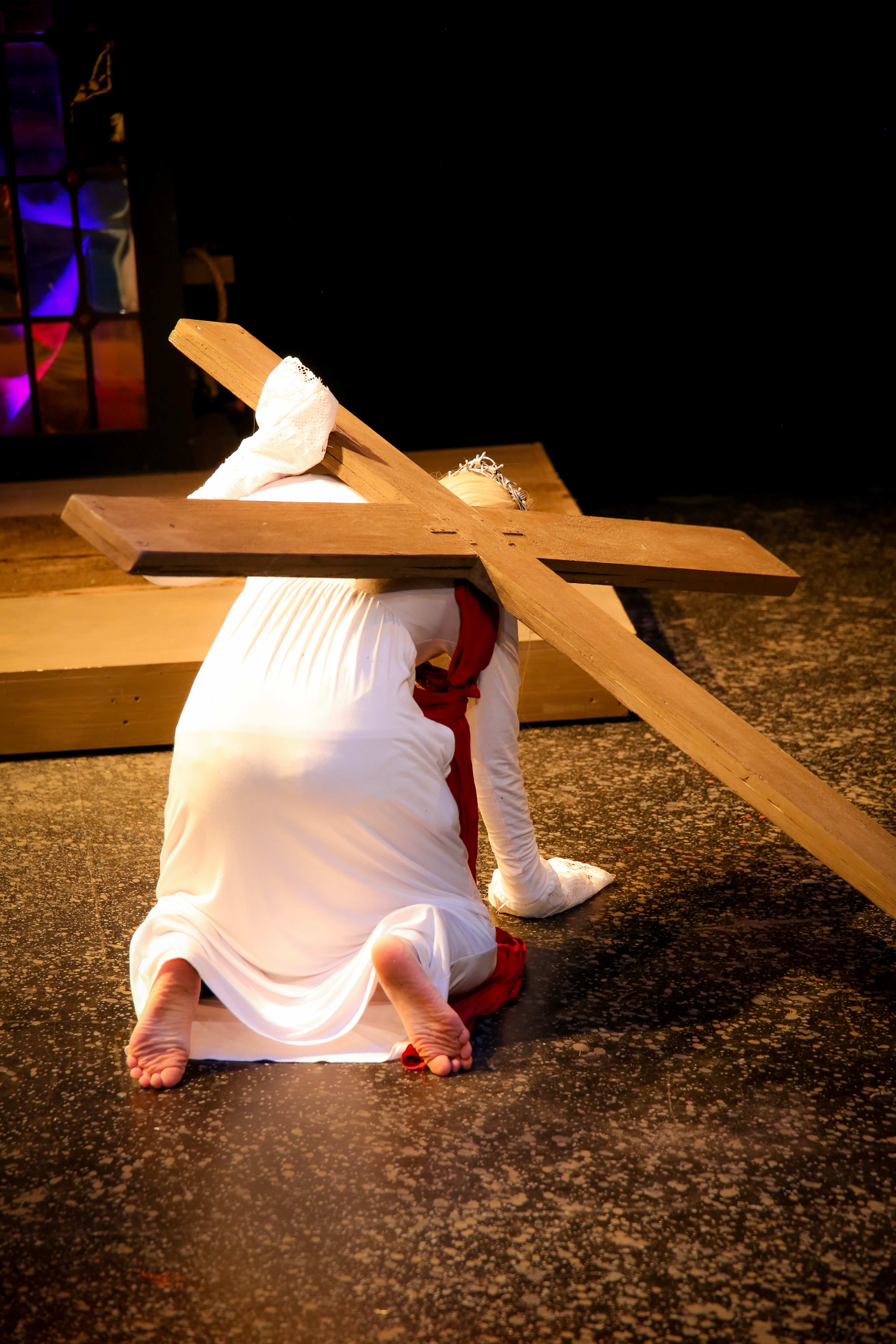 The Pillowman - Figure in white carrying wooden cross, kneeling