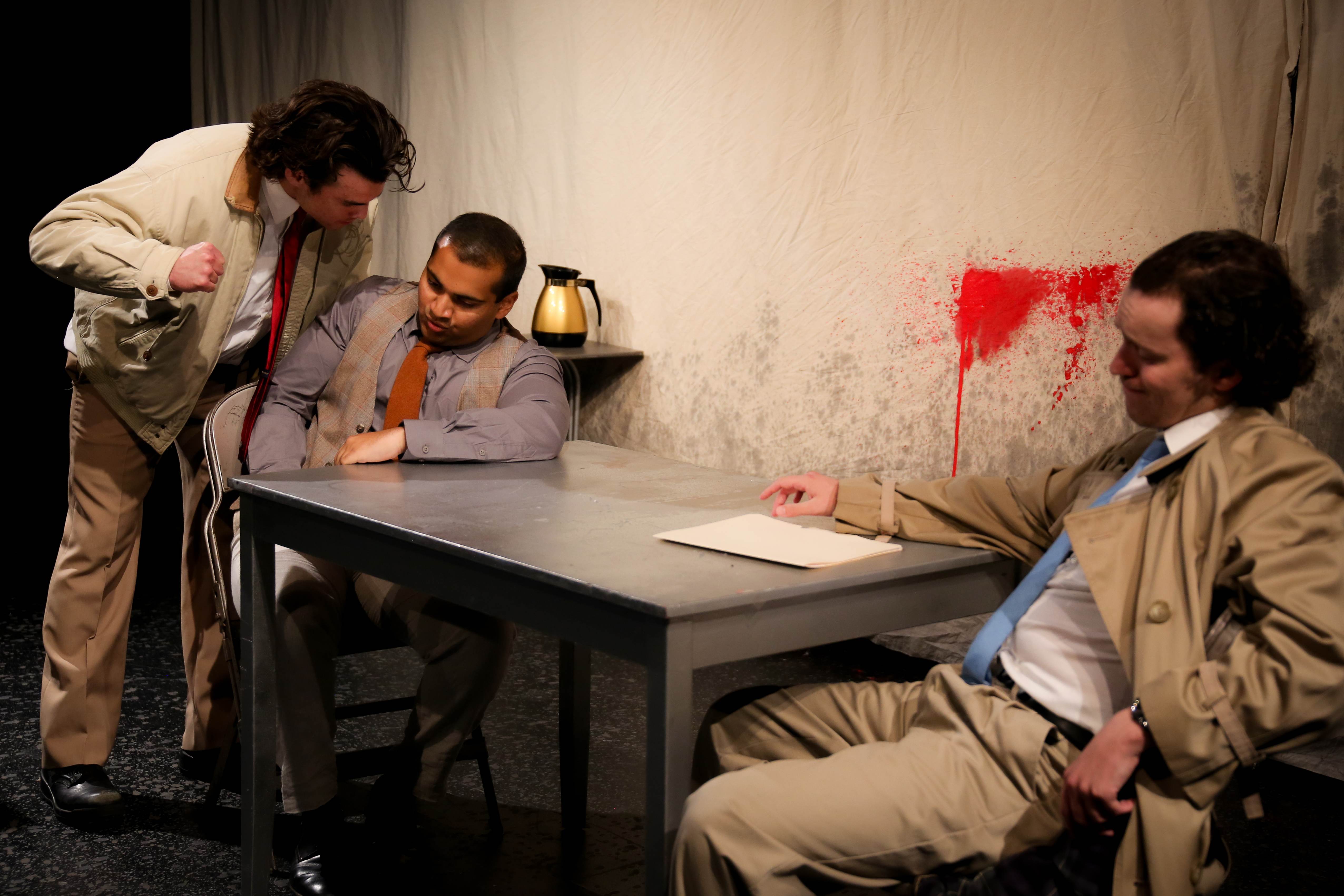 The Pillowman - Three men at interrogation table with blood-splattered wall