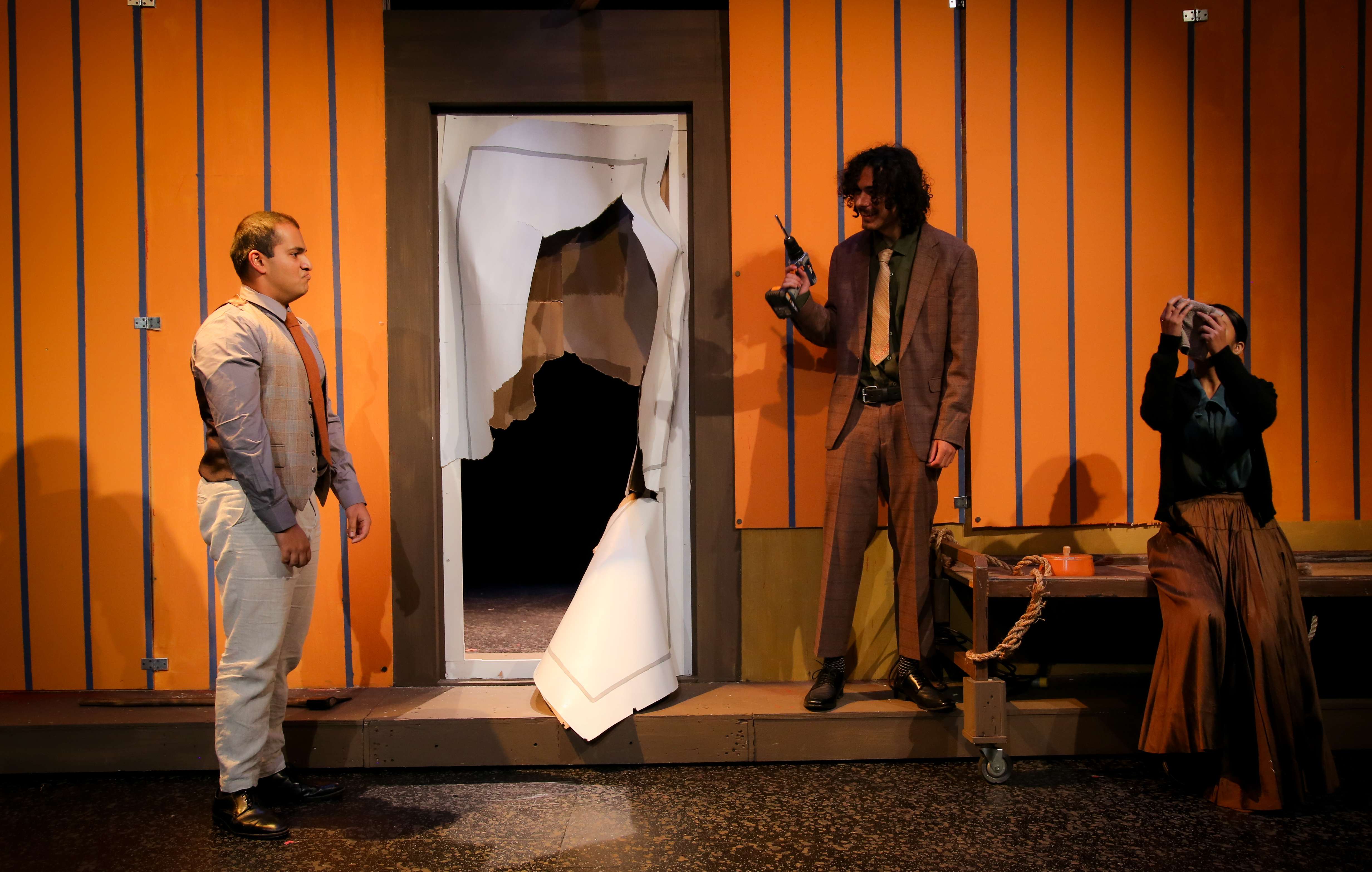 The Pillowman - Three actors with drill against orange striped walls