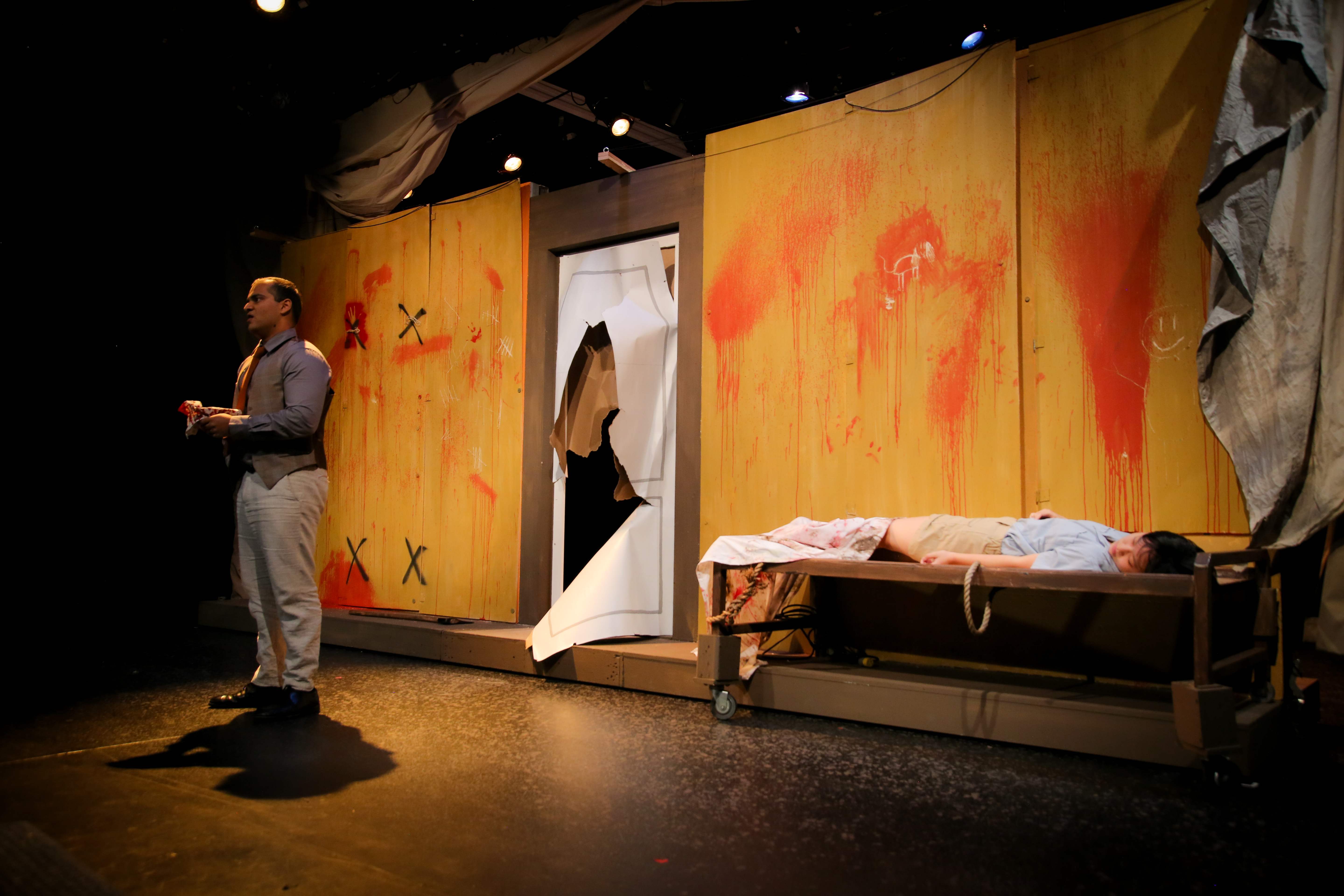 The Pillowman - Wide stage with blood-splattered walls and torn door